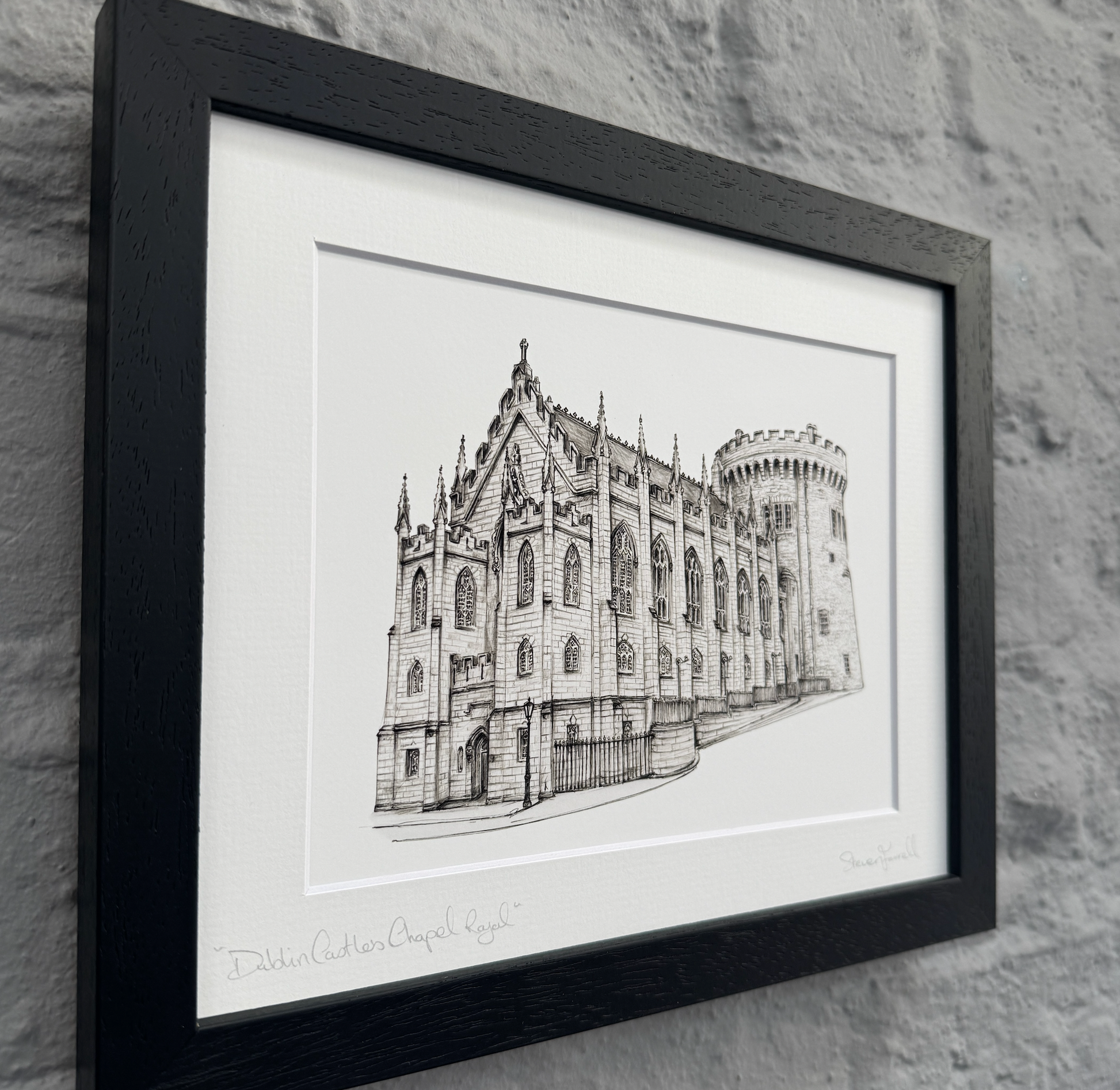 Framed black and white architectural drawing of a building on a stone wall background