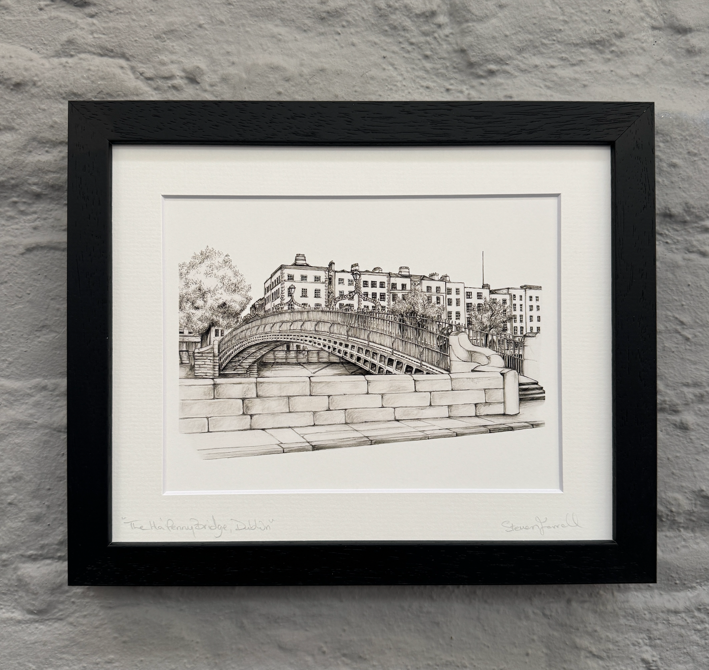 Framed black and white print of a bridge and buildings on a stone wall.