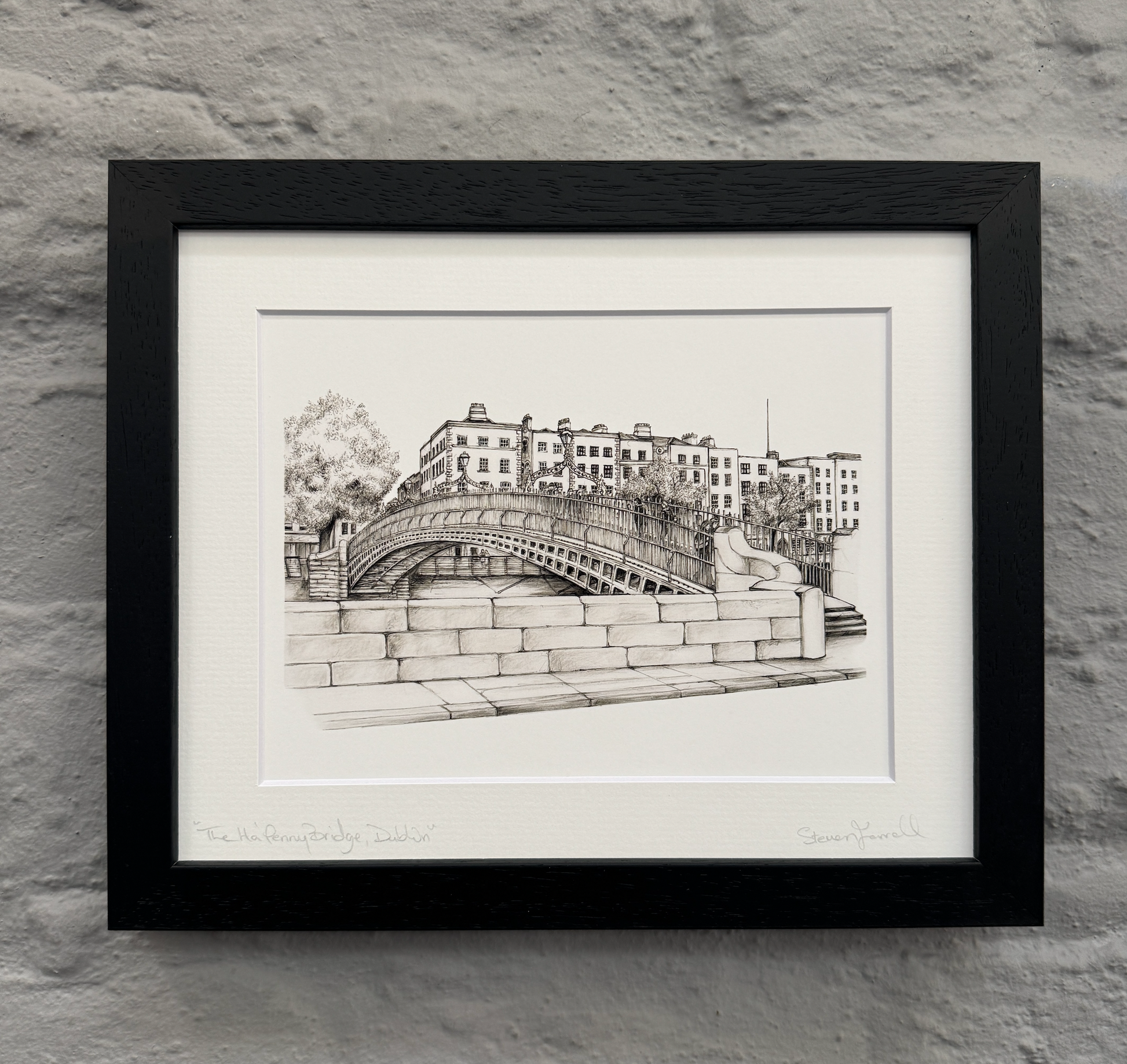 Framed black and white print of a bridge and buildings on a stone wall.